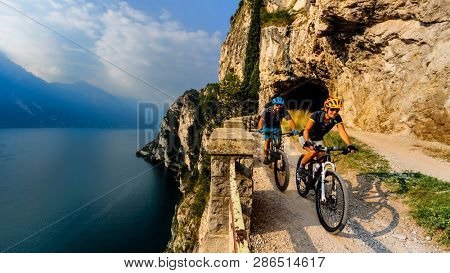 Cycling woman and man riding on bikes at sunrise mountains and Garda lake landscape. Couple cycling MTB enduro flow sentiero ponale trail track. Outdoor sport activity.