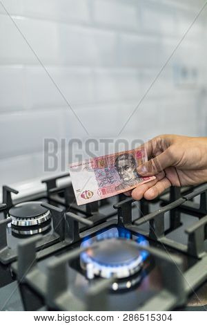 Cooktop With Burning Gas Ring With Hands Holding Money 10 Uah Hryvnas For Combustion At Home.
