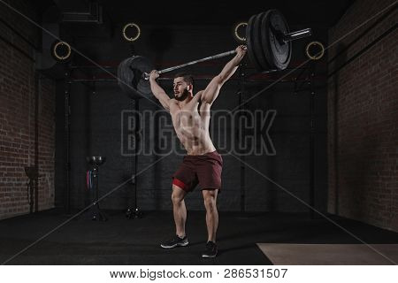 Young crossfit athlete lifting heavy barbell overhead at the gym. Handsome man doing functional trai