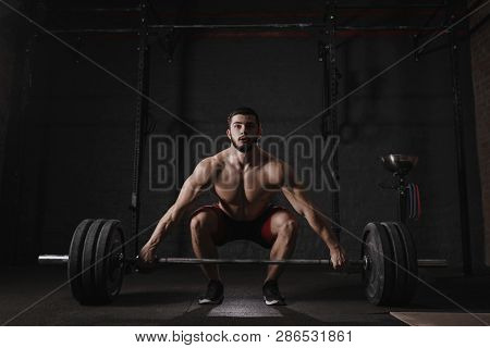Young crossfit athlete lifting barbell at gym. Muscular shirtless man doing functional training. Dea