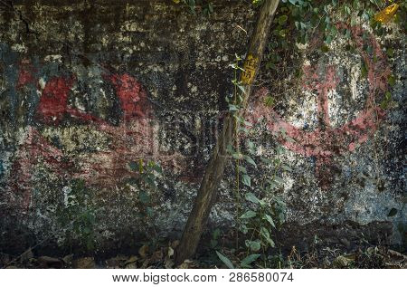 Old Weathered Dilapidated Wall Covered With Plants, With The Image Of A Sickle And Hammer