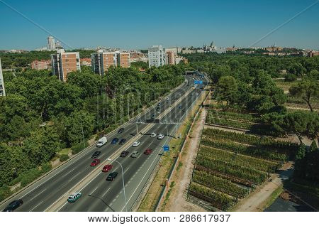 Multi-lane Highway With Heavy Traffic In The Midst Of Garden Trees And Apartment Buildings, In A Sun