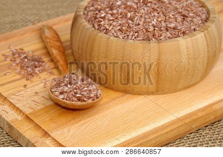Uzbek Devzira, The Red Rice In A Bamboo Bowl And A Wooden Spoon On A Cutting Board Closeup