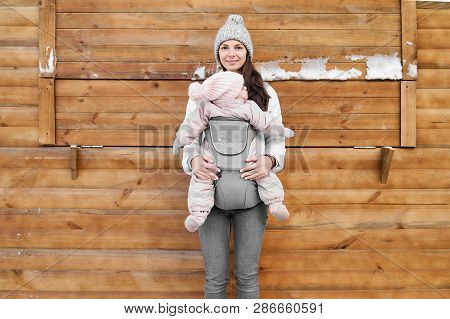 Little Baby Girl And Her Mother Babywearing The Ergo Carrier In Winter Wooden Background