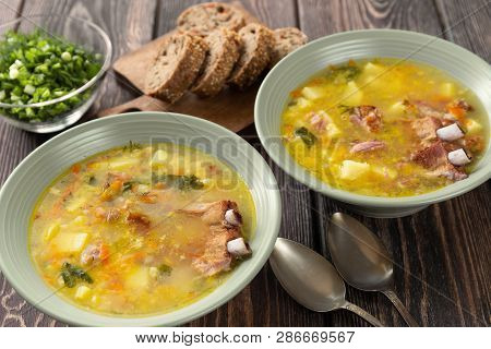 Two Plates Of Delicious Yellow Split Peas Soup With Smoked Pork Ribs  On A Wooden Table.