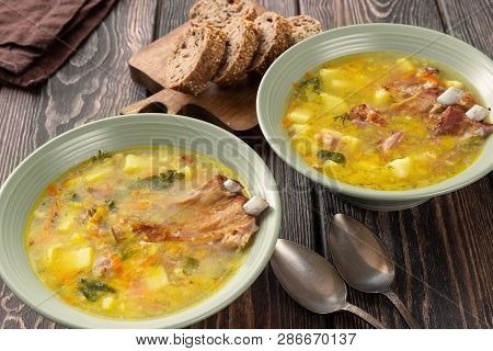 Two Plates Of Delicious Yellow Split Peas Soup With Smoked Pork Ribs  On A Wooden Table.