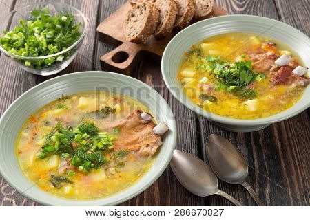 Two Plates Of Delicious Yellow Split Peas Soup With Smoked Pork Ribs  On A Wooden Table.