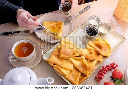 Woman Is Eating Russian Traditional Pancakes, Blini Served With Jams, Sour Cream, And Strawberry On 