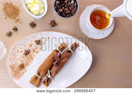 Pouring Tea In Cup From Teapot. Chocolate Russian Pancakes, Blini With Curd Filling On The Plate.