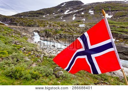 Norwegian Flag Waving On Wind And Camper Car In Mountains In The Background. Travel, Holidays And Ad