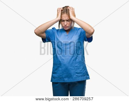 Young caucasian nurse woman wearing surgeon uniform over isolated background suffering from headache desperate and stressed because pain and migraine. Hands on head.