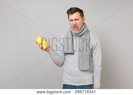 Abhorred Young Man In Gray Sweater, Scarf Holding Lemons Isolated On Grey Wall Background, Studio Po