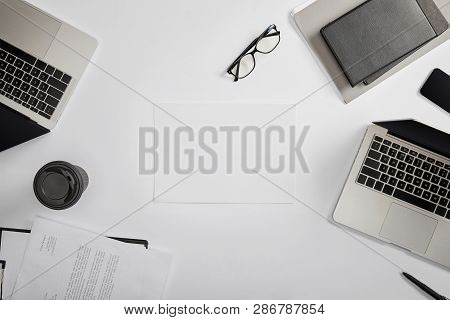 Top View Of Documet On Clipboard, Paper Cup, Laptops, Pen, Notebooks, Folder, Glasses And Blank Pape