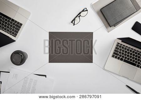 Top View Of Documet On Clipboard, Paper Cup, Laptops, Pen, Notebooks, Folder, Glasses And Grey Paper