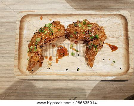 Top View Of Fried Chicken Wings With Spicy Sauce Topped With Scallions Sliced On Wooden Plate (yangn