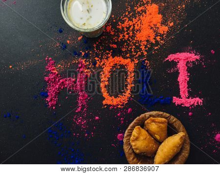 'HOLI' word written by power color along with holi special sweet- Gujia and Bhaang milk. Indian festival Holi Greetings background photo.