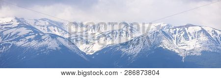 Panorama of a mountain range with snowy peaks. Spring landscape with melting snow in the mountains
