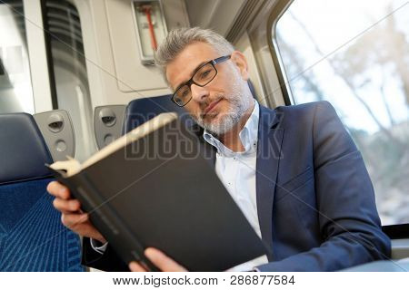 Businessman going to work by train, reading book