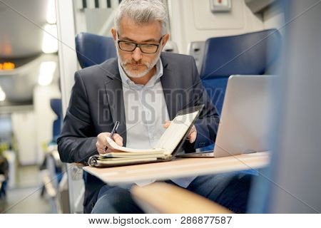 Mature businessman working on laptop while traveling in train 