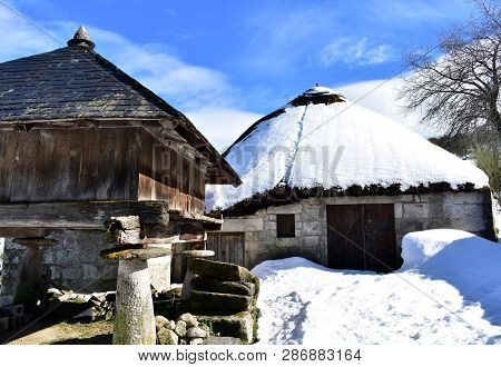 Ancient snowy palloza house and wooden horreo granary (galician granary). Piornedo, Ancares, Galicia, Spain.