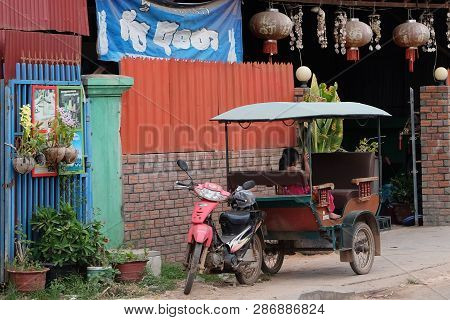 Cambodia, Siem Reap 12/08/2018 A Little Asian Girl Sits In A Moto Rickshaw Near A House With Red Lan