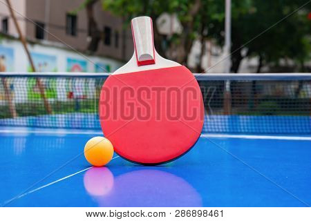 Pingpong Racket And Ball And Net On A Blue Pingpong Table In A Park