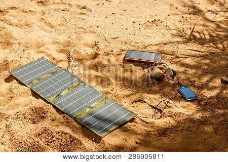 Solar Panel Lying On The Ground And Charges The Smart Phone, The Sahara Desert. Charge Smart Phone F