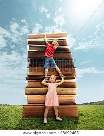 Little Girl And Boy Climbing On The Tower Made Of Big Books. Childhood Dreams, Reading And Education