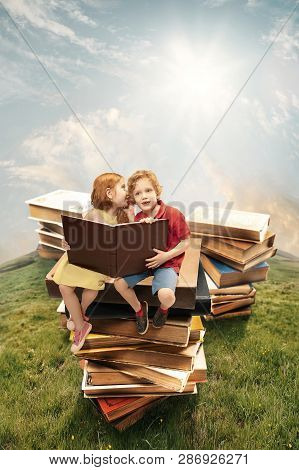 Little Girl And Boy Sitting On The Tower Made Of Big Books. Childhood Dreams, Creative And Education