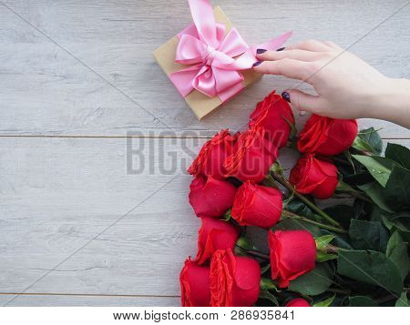 Preparing A Gift, On A Wooden Table, With Roses. Female Hand Holding A Gift, Wrapped With Ribbon, On