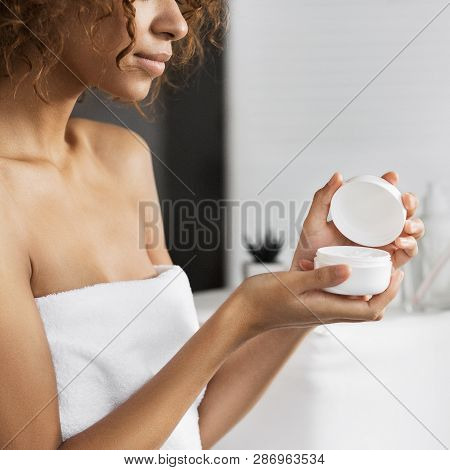 Afro-american Girl Holding Cream In Bathroom, Reflecting In Mirror. Intence Body Cream Concept
