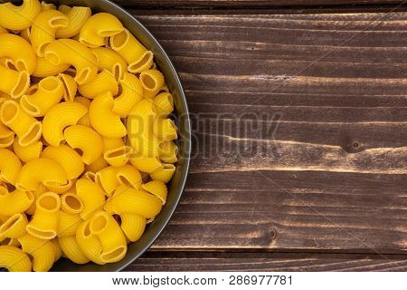 Closeup Of Lot Of Whole Raw Pasta Pipe Rigate Variety In A Grey Ceramic Bowl Flatlay On Brown Wood