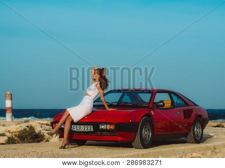 Young Beautiful Girl In Sunglasses Sitting On The Hood Of The Red Ferrari