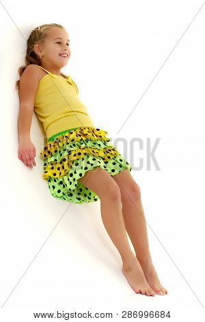 A Cute Little Girl Leaned Against A White Wall. Cyclorama In Studio. Isolated On A White Background.