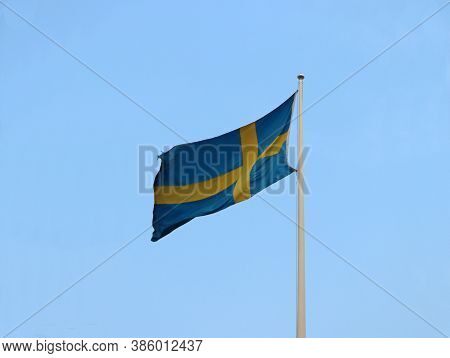 Two Color Of Swedish Flag, Yellow Cross On Blue Color On Blue Sky Background. Blown Away By Wind.