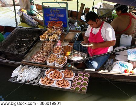 Amphawa, Thailand, January 23, 2016: Cook Checks His Phone In His Barbecue Boat Full Of Seafood At A