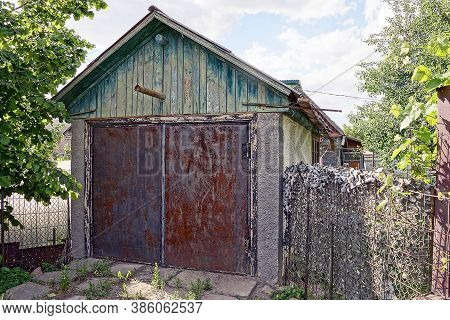 Rural Old Garage With Wooden Loft And Iron Red Rusty Gates On The Street