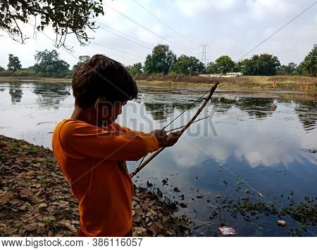 District Katni, India - January 01, 2020: An Asian Village Kid Pointing Bow Arrow Shot Towards Water