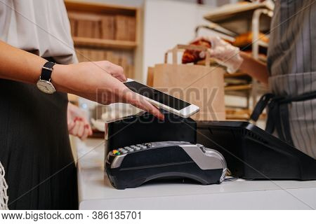 Woman In A Bakery Shop Making A Purchaise, Paying With Her Phone
