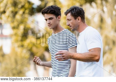 Father Gesturing And Talking With Teenager Son In Park