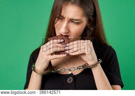 Sugar Addiction Concept. Caucasian Young Woman In Handcuffs Is Biting A Chocolate Bar. Isolated On G