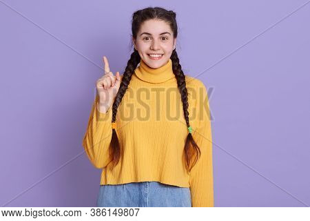 Smiling Brunette Female With Pigtails Looking Directly At Camera With Index Finger, Wearing Yellow S
