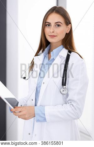 Doctor Woman Using Tablet Computer While Standing Straight Near Window In Hospital. Happy Physician 