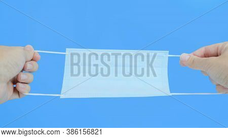 A Person Holding And Straitening A Sirgical Medical Protective Mask In Order To Put It On, View From