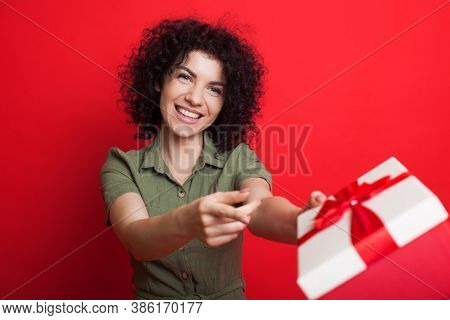 Charming Curly Haired Woman Smiling And Giving A Present At Camera Gesturing With Finger That Is Is 