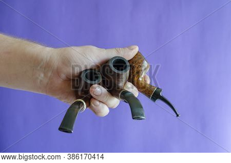 A Male Hand Holds Three Smoking Pipes On A Blue Background. Occasional Smoking Pipes Bend From Heath