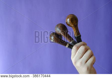 A Male Hand Holds Three Smoking Pipes On A Blue Background. Occasional Smoking Pipes Bend From Heath