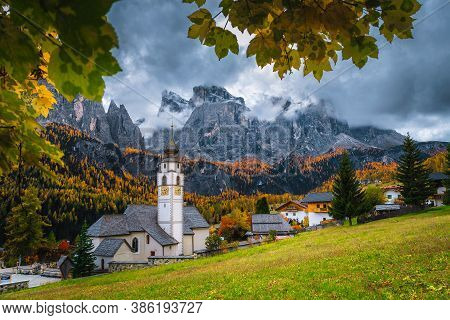 Amazing Autumn Scenery With Colorful Larch Forest. Charming Alpine Village With Beautiful Church. Gr