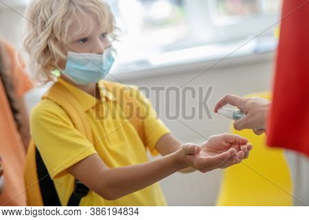 Blonde Boy In Preventive Mask Disinfecting His Hands While Enetering The School