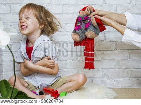 The Child Plays On The Floor With Bare Feet. Womens Hands Stretch Out Warm Clothes - Socks And A Sca